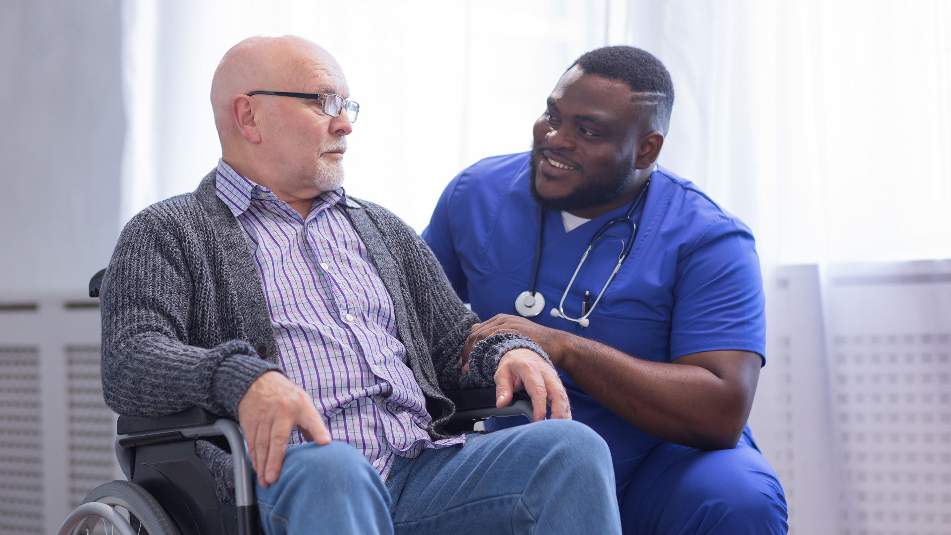 Symbolbild: Pfleger kümmert sich um einen Rollstuhlfahrer