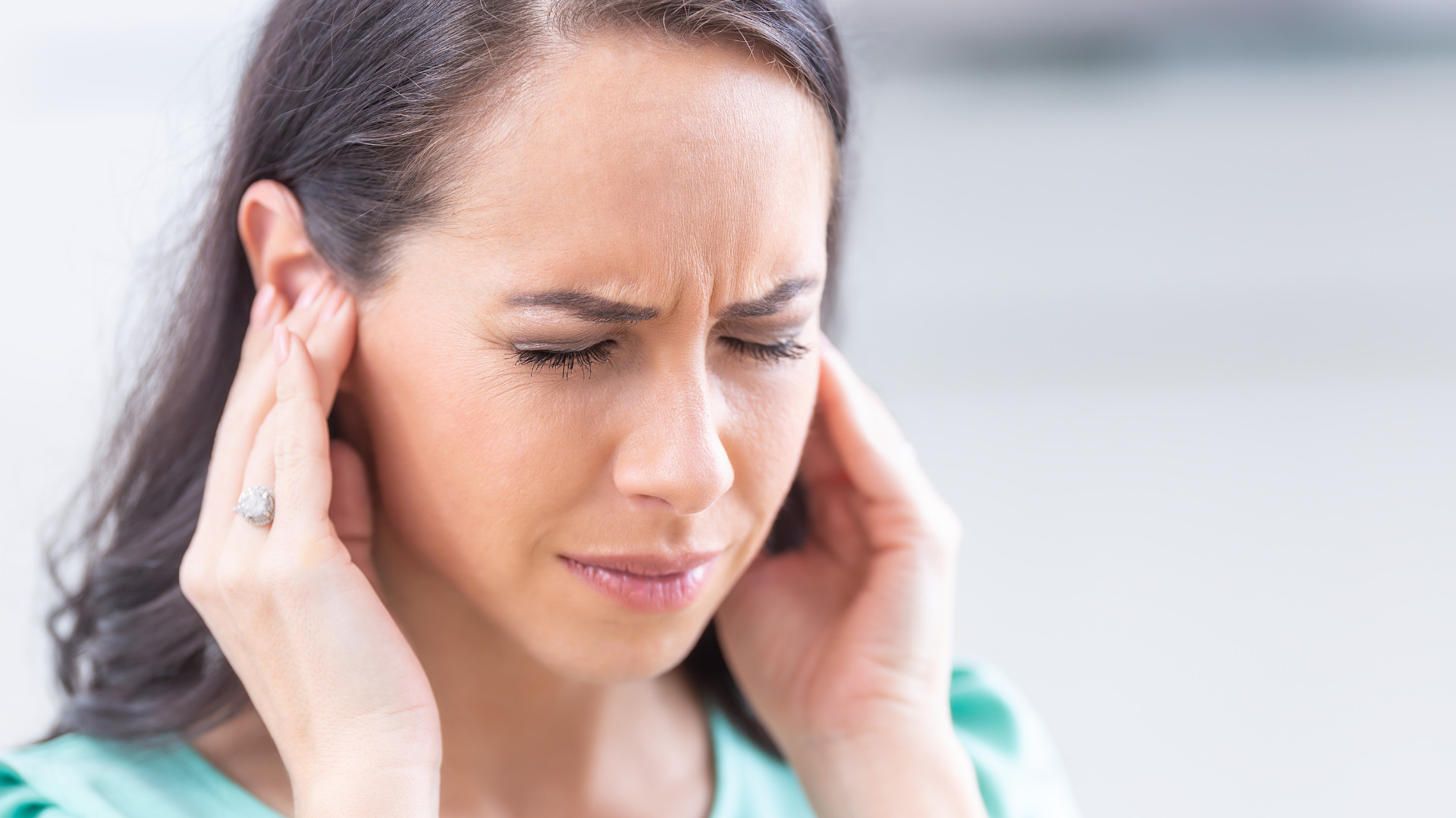 Symbolbild: Frau hält sich mit schmerzverzehrendem Gesicht die Ohren