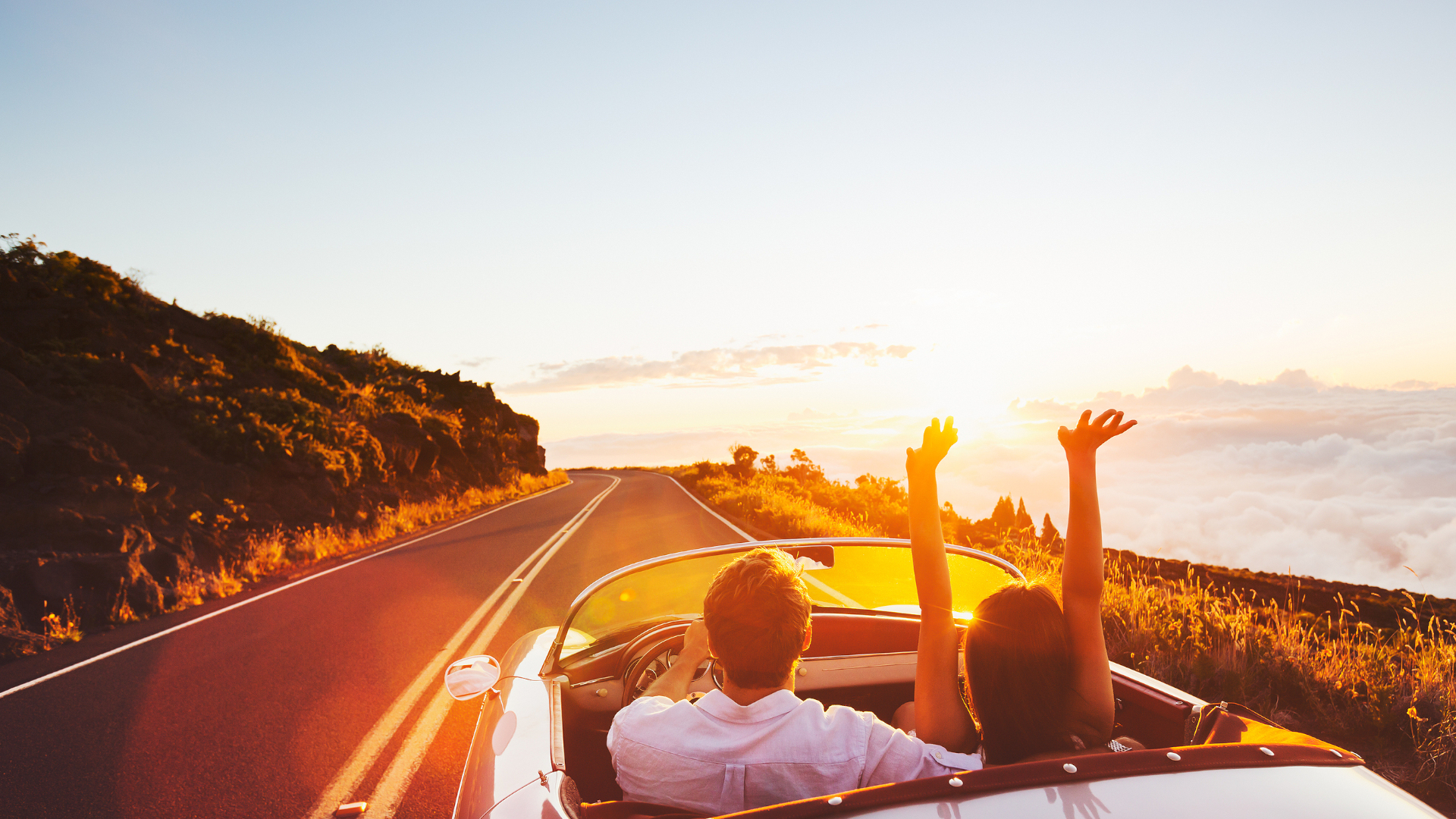 Symbolbild: Paar fährt mit einem Cabrio in den Sonnenuntergang
