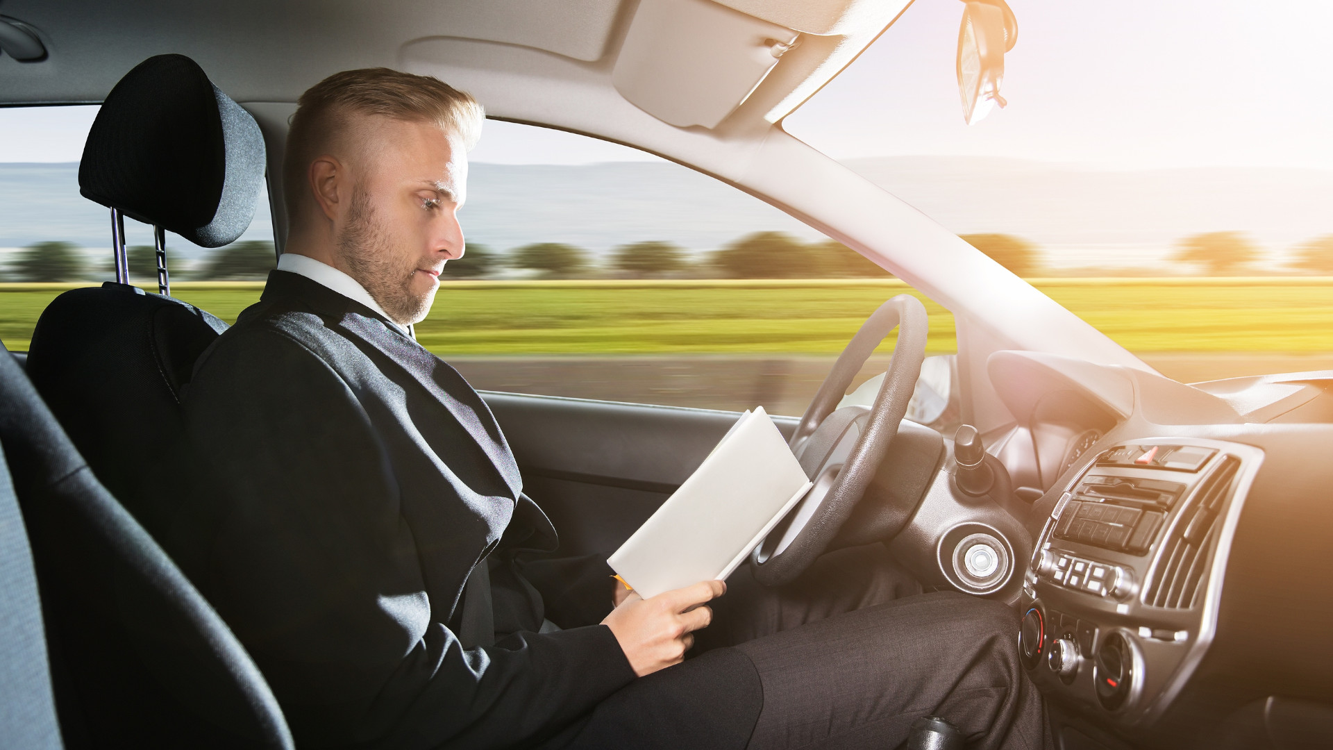 Symbolbild: Mann sitzt im Fahrzeug und liest sein Buch, während das Auto von selbst fährt.