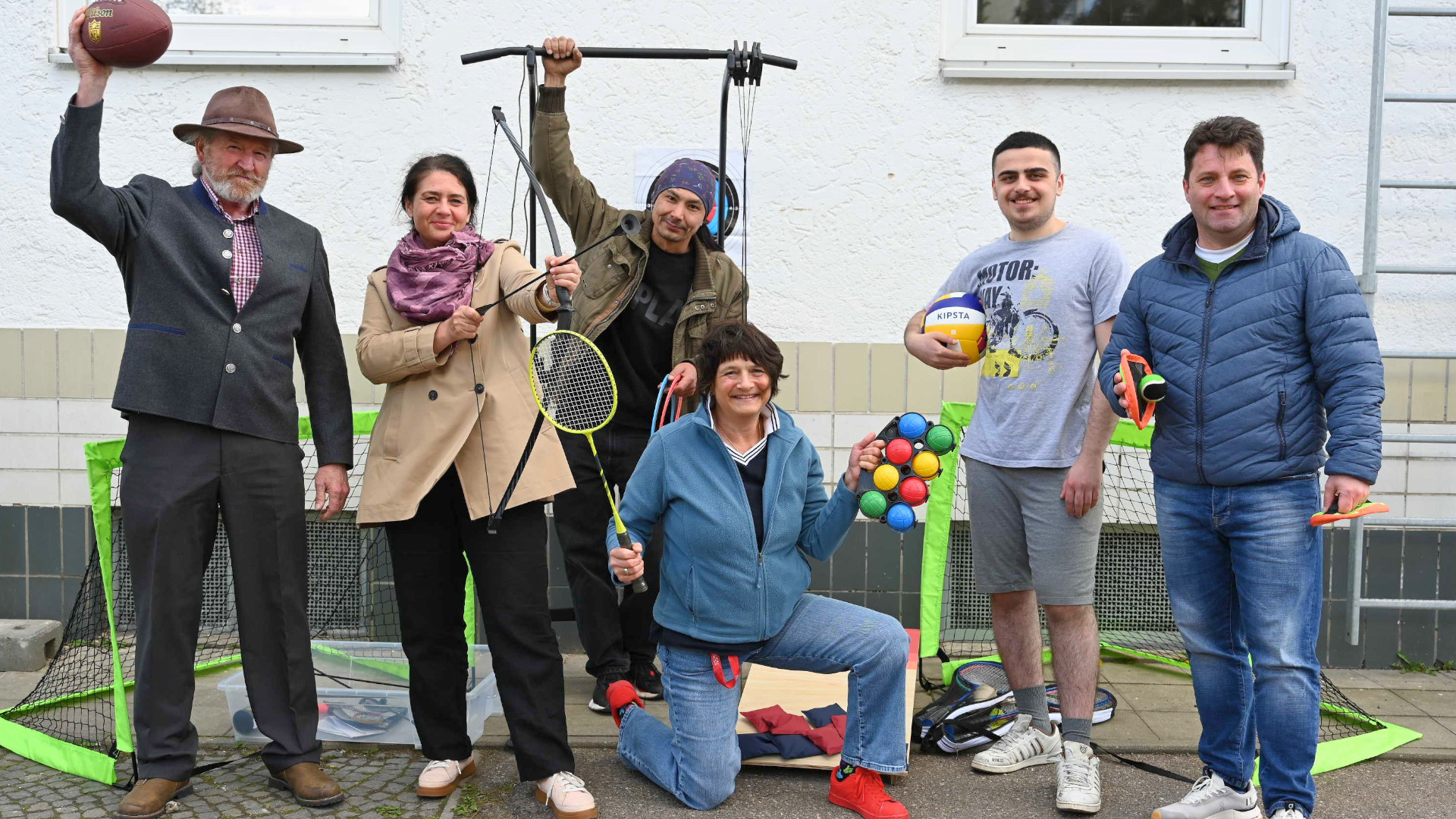  Jack Bryant (li.), 2. Vorsitzender, und Schriftführer Hugo Wagner  (re.) von Maroni Wunschbaum e.V. übergeben im Innenhof der Caritas Notunterkunft NOAH-deinTagNachtHalt die Sportartikel an Einrichtungsleiterin Barbora Pokorny (2.v.li.) und Betreuungsassistentin Anette Bayer (3.v.re.). Zwei Bewohner der Notunterkunft sind ebenfalls dabei.