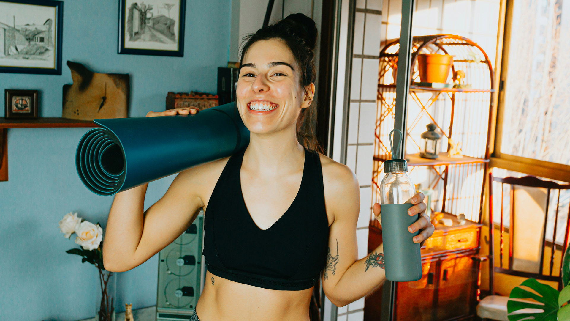 Lächelnde Frau im Sportoutfit mit Yogamatte über den Schultern