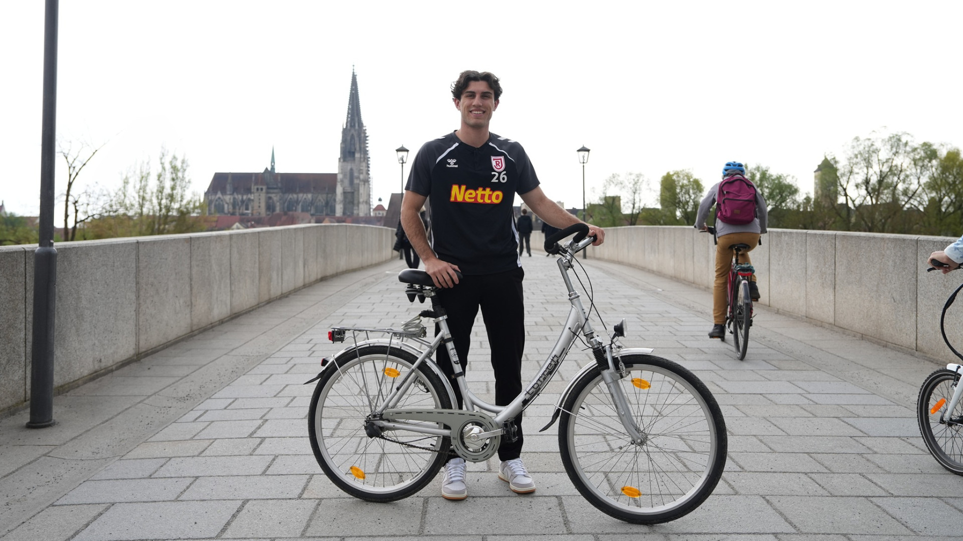 Fußballer steht mit seinem Rad auf der Steinernen Brücke