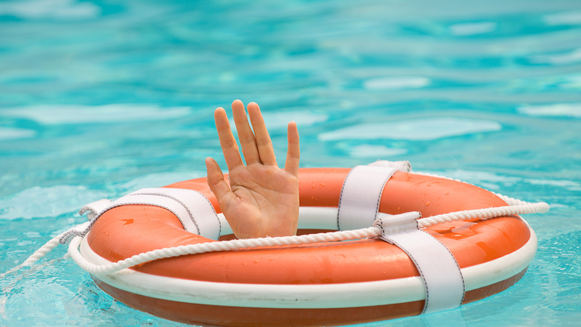 Symbolbild: Rettungsring treibt im Wasser, während eine Hand versucht, sich daran festzuhalten