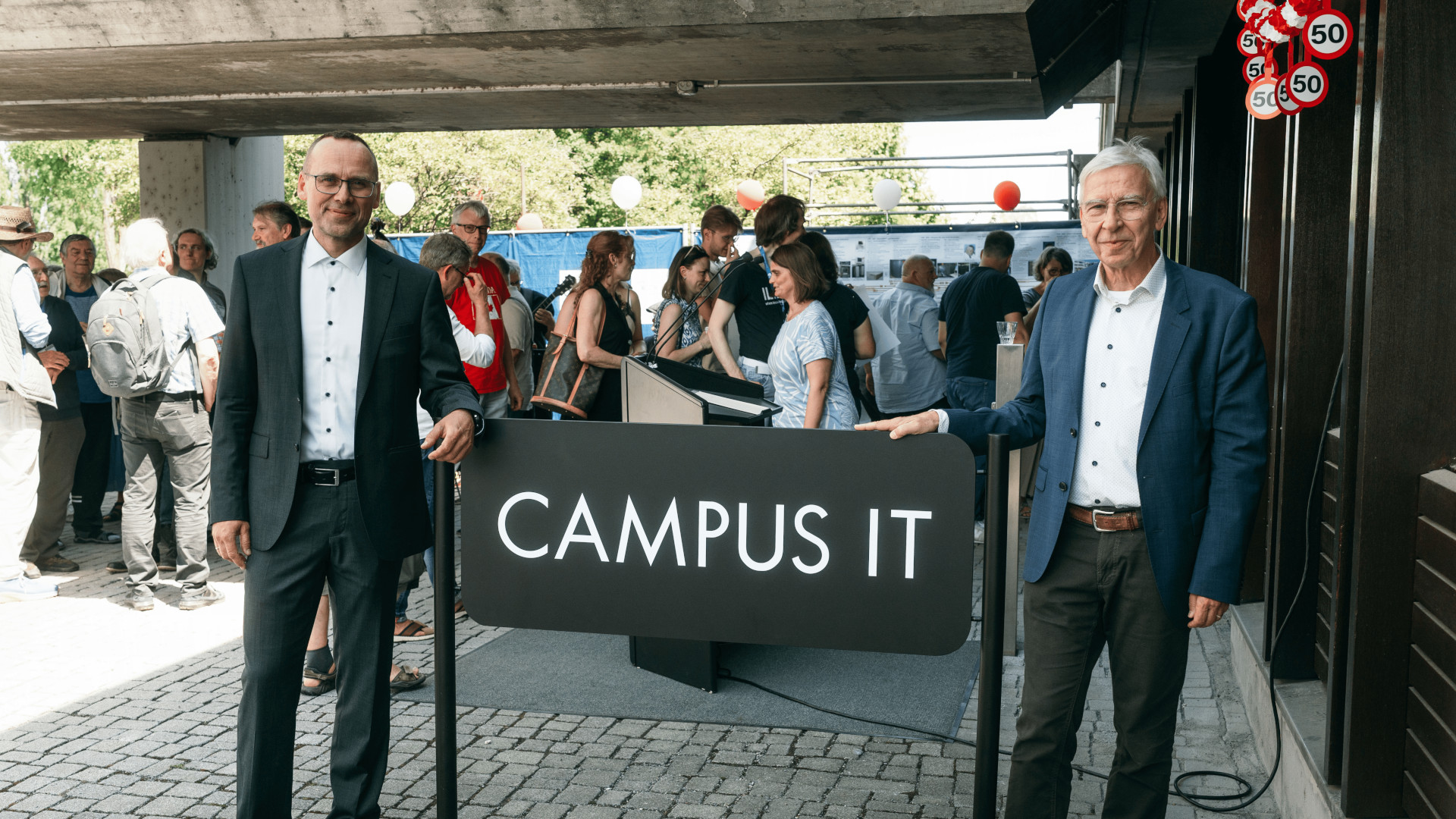 (li.) Dr. Christoph Bauer, Leiter der Campus IT und Universitätspräsident Prof. Dr. Udo Hebel (re.) enthüllen das Schild mit dem neuen Namen "Campus IT"