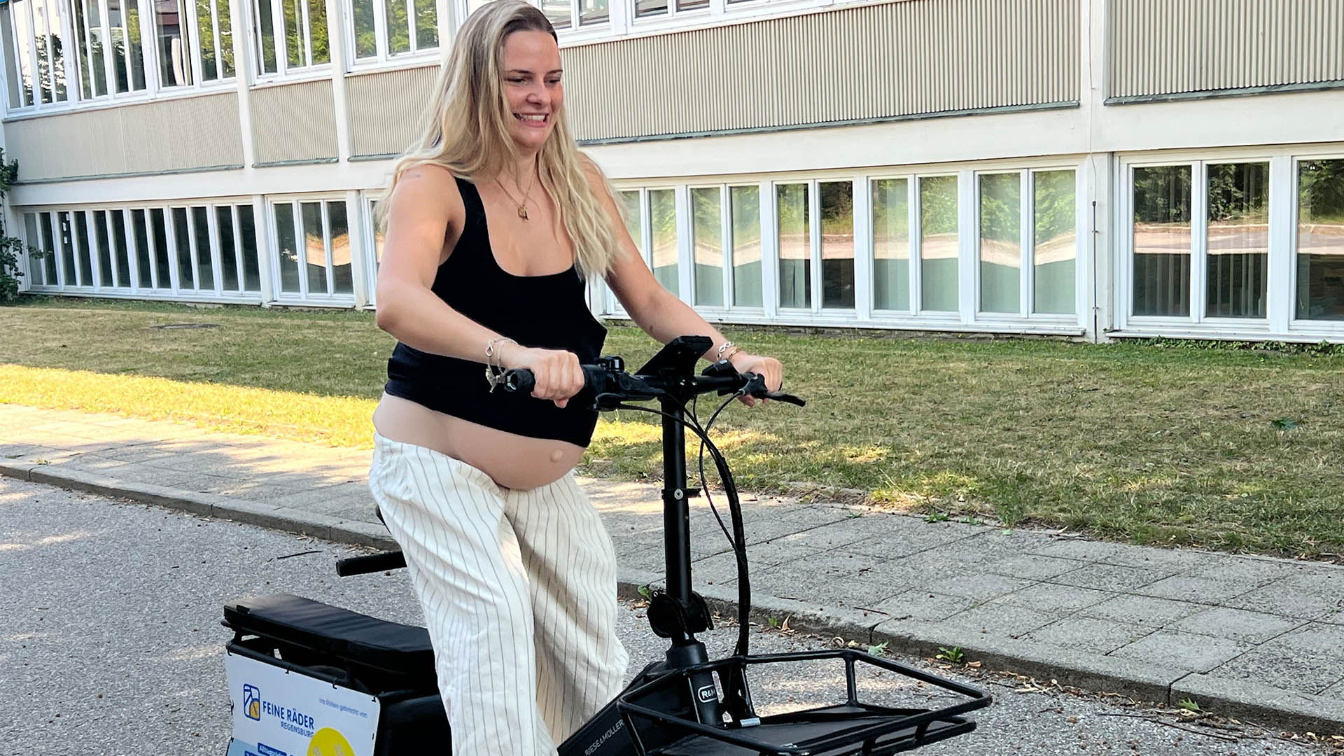 Hebammenstudentin der OTH Regensburg testet mit einem umgebundenen Schwangerschaftsbauch ein Longtail-Lastenfahrrad 