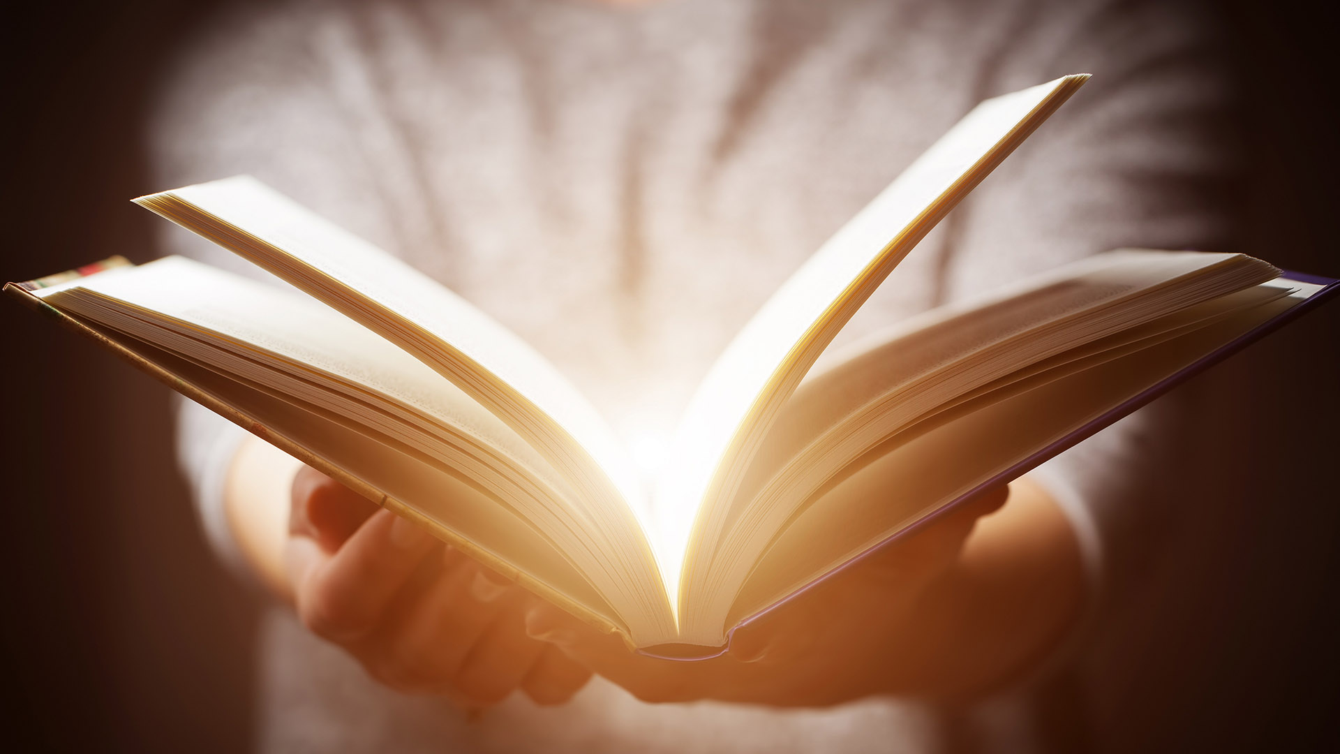 Junge schlägt Buch auf, das im Innernen leuchtet und magisch erscheint