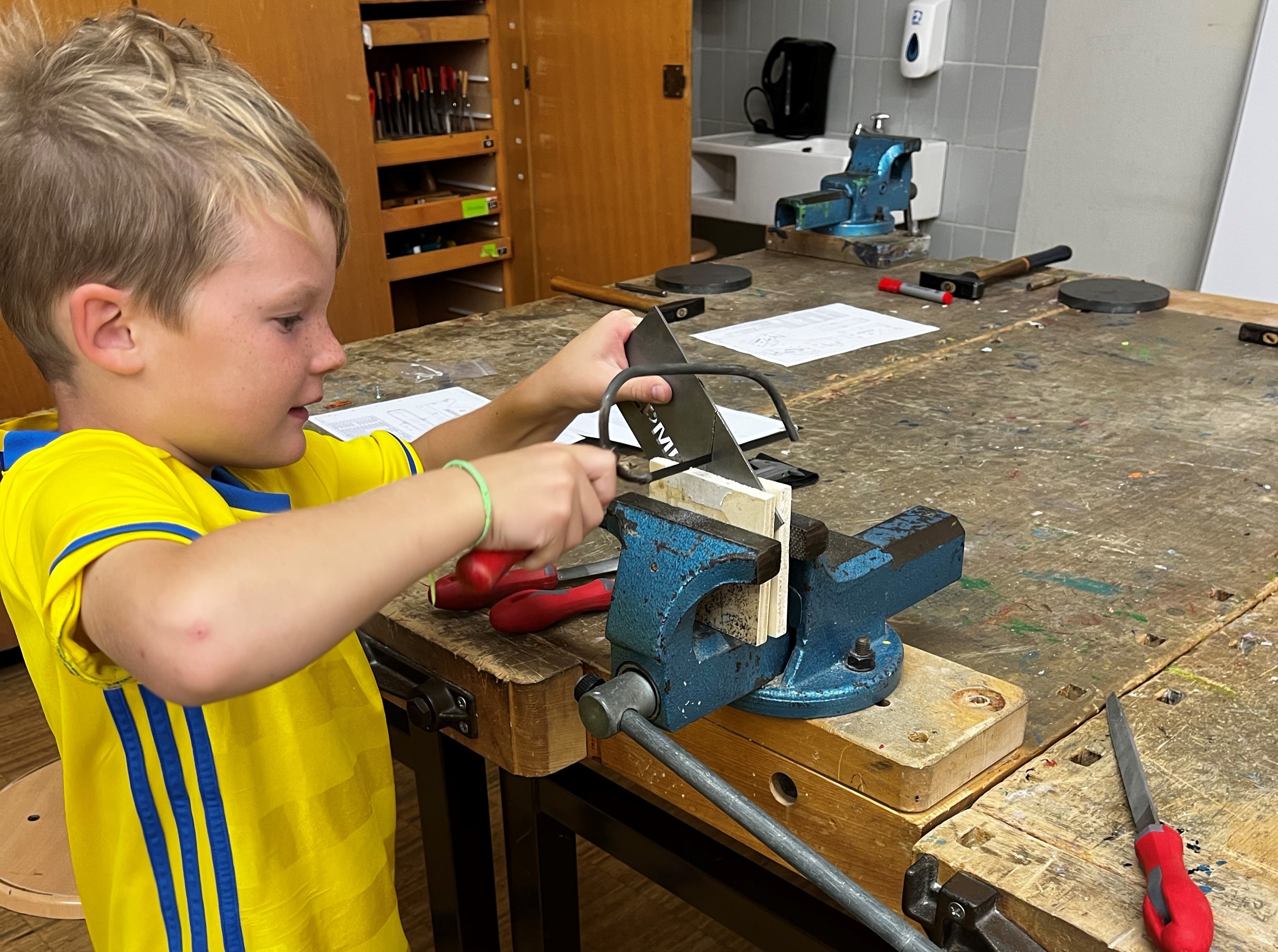 Junge schneidet Holz im Schraubstock durch