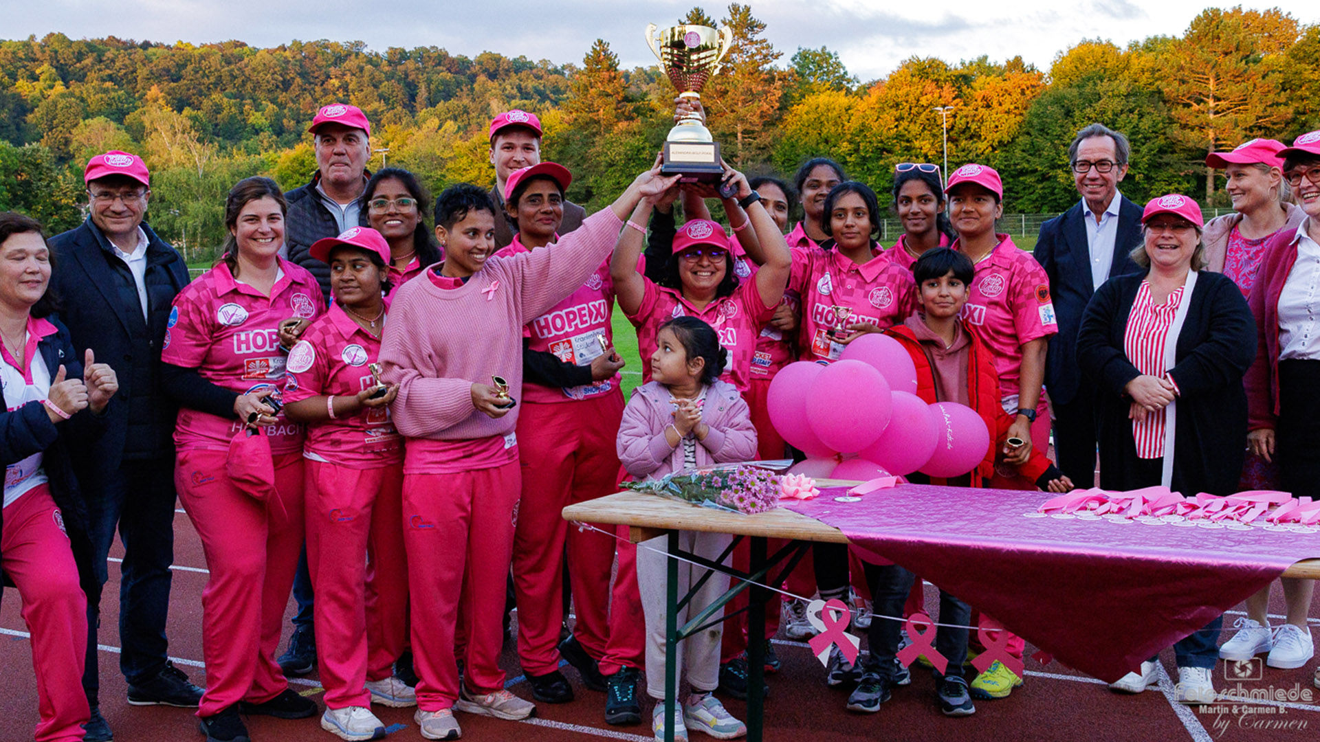 Pink Lady Cricket: Frauen in Pink jubeln, eine in der Mitte hält einen Pokal hoch.