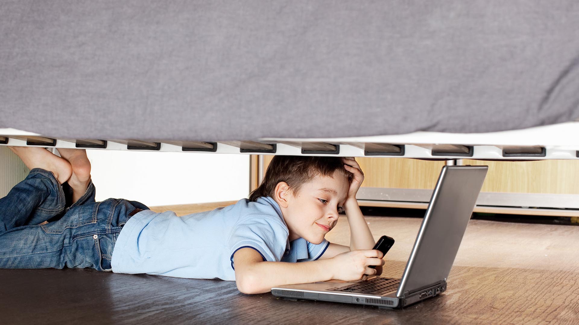 Junge mit Laptop unterm Bett