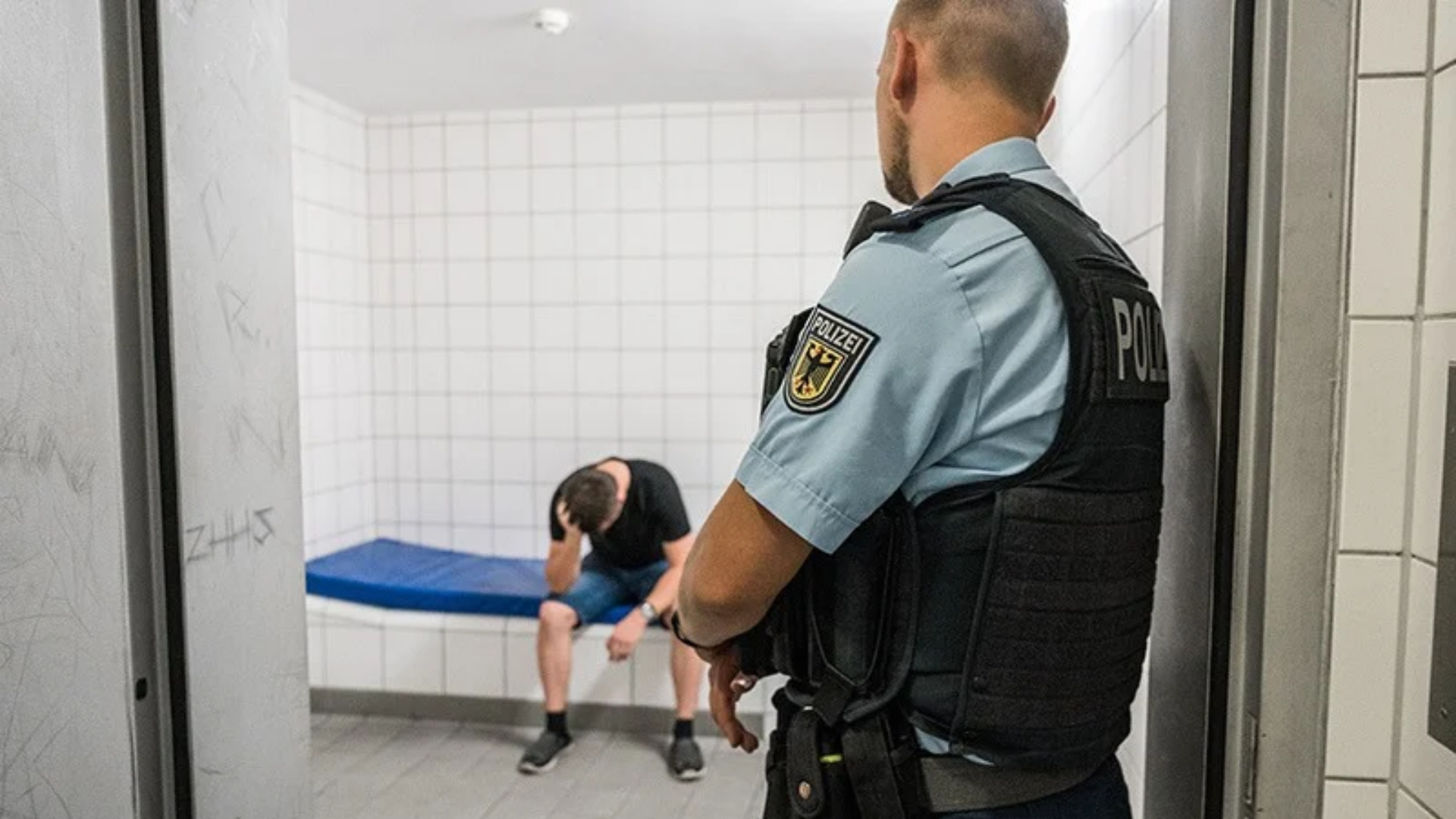 Ein Mann in einer Zelle, ein Polizist steht an der Tür